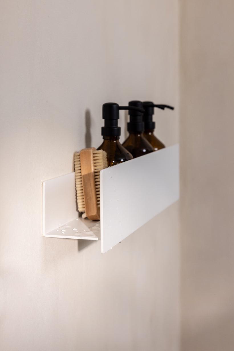 Duschablage SHEA mit Shampoo-Flaschen und einer Bürste auf einer weißen Wand, stilvolles und praktisches Badezimmerregal.